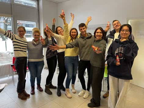 Groep studenten viert binnen feest, glimlacht en houdt kleine chocolade kerstmannen vast.