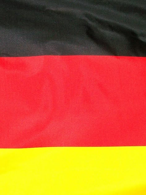 La imagen muestra la bandera alemana desde muy cerca. Se aprecian los colores negro, rojo y dorado típicos de Alemania.