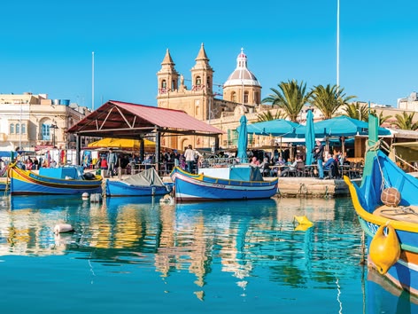 Kleurrijke vissersboten en cafés aan het water op de markt van Marsaxlokk in Malta.