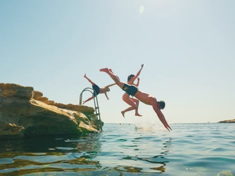 Groep tieners springt in zee vanaf rotsen op een zonnige dag.