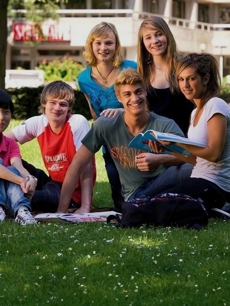 Groepje Sprachcaffe junior studenten op het gras in Frankfurt, Duitsland, lachend en genietend van een zonnige dag.