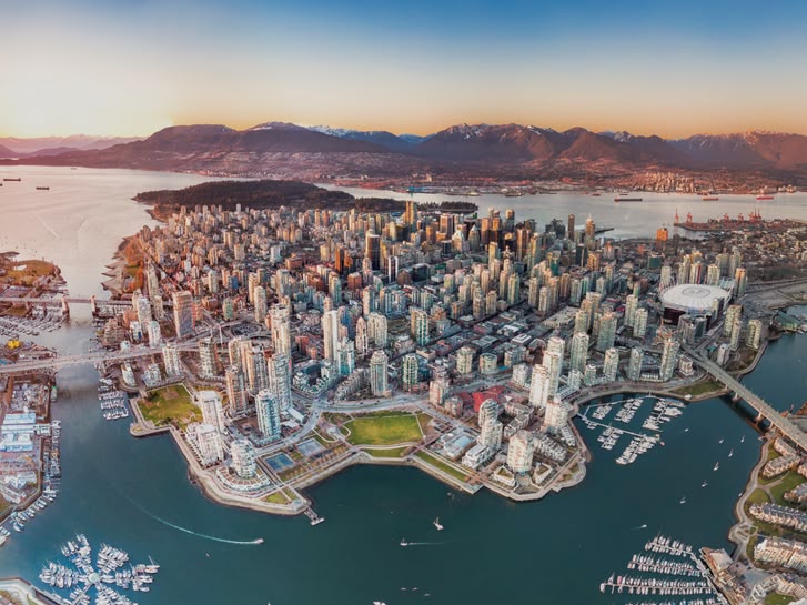 Luchtfoto van het centrum van Vancouver, Canada, met omliggende bergen, havens en bruggen bij zonsondergang.