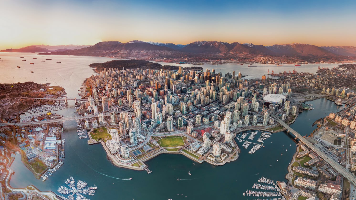 Luchtfoto van het centrum van Vancouver, Canada, met omliggende bergen, havens en bruggen bij zonsondergang.
