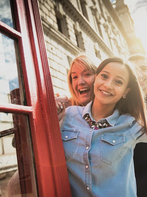 Lachend meisje poseert bij een rode telefooncel in Londen met de Big Ben op de achtergrond.
