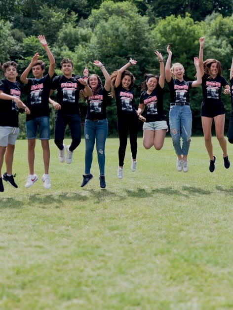 Sprachcaffe studenten in Engeland springen in de lucht op een groen veld, dragen bijpassende shirts en genieten van de buitenlucht.