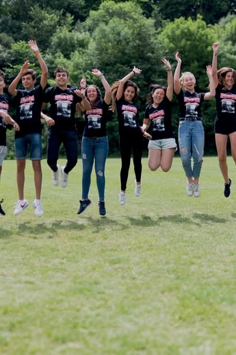 Sprachcaffe studenten in Engeland springen in de lucht op een groen veld, dragen bijpassende shirts en genieten van de buitenlucht.