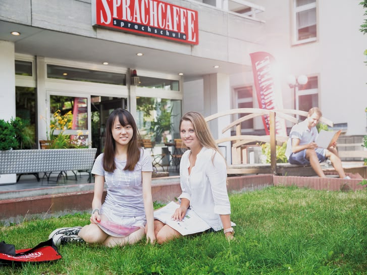 Twee jonge vrouwen zitten op het gras voor de Sprachcaffe taalschool in Frankfurt, Duitsland.