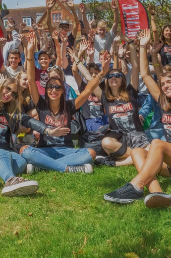 Groep Sprachcaffe-studenten zit op het gras in Londen, glimlacht en steekt de armen omhoog tijdens een buitenactiviteit.