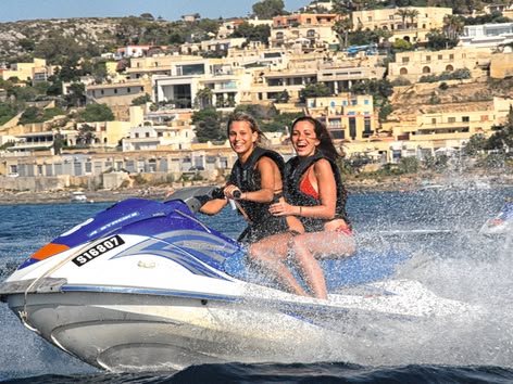 Twee jonge vrouwen lachen terwijl ze op een jetski langs de kust van Malta rijden.