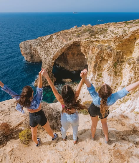 Drie meisjes die hun armen omhoog houden op kliffen met uitzicht op de Blauwe Grot.