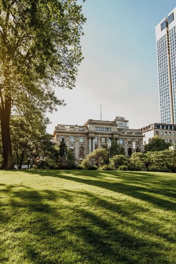 Zonnig park in Frankfurt, Duitsland, met moderne wolkenkrabbers en groene open ruimte op de voorgrond.